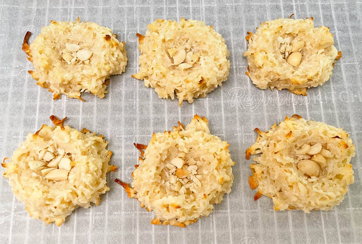 Baked coconut macaroons with macadamia nuts in the bottom of the well sitting on a parchment paper covered rack.