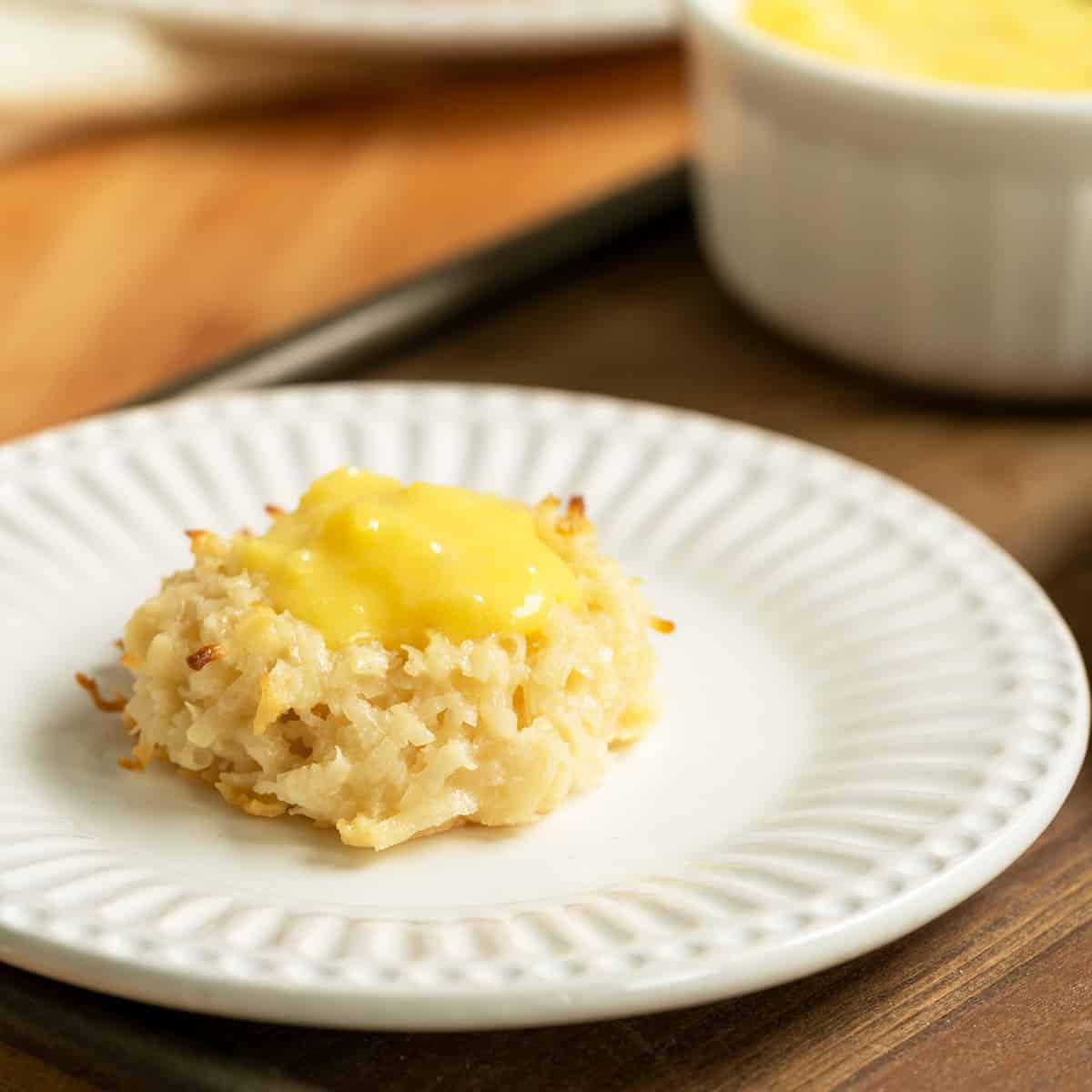 Creamy coconut pineapple macaroon on a white plate with a white container of pineapple curd.