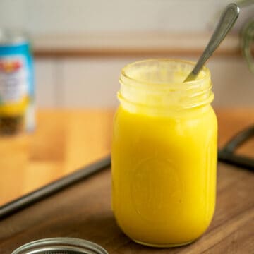 Creamy Pineapple Curd in a jar with a spoon on a wooden tray.
