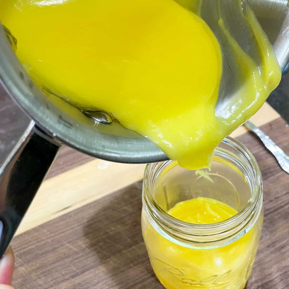 Pouring pineapple curd into a glass jar.