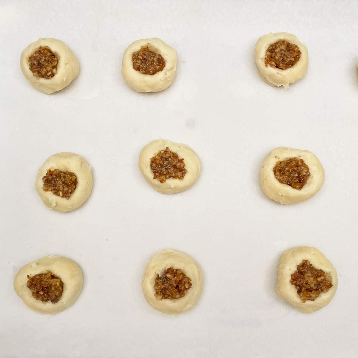 Nine round cookies with walnut date filling in the middle on parchment paper before they are baked.