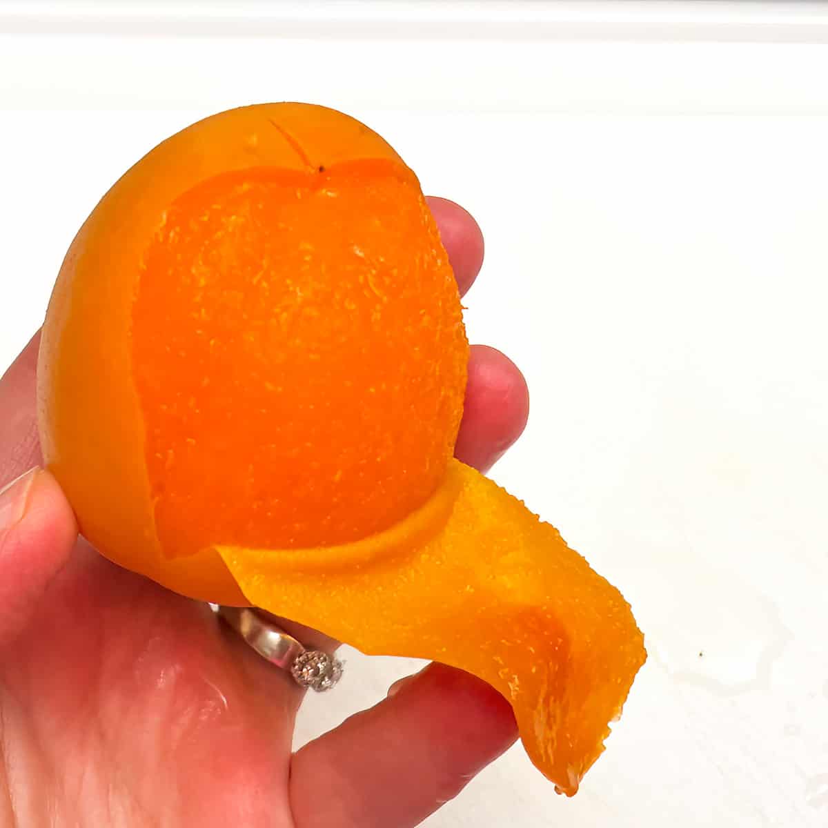 Peeling an apricot after the ice bath by scored cross on top.