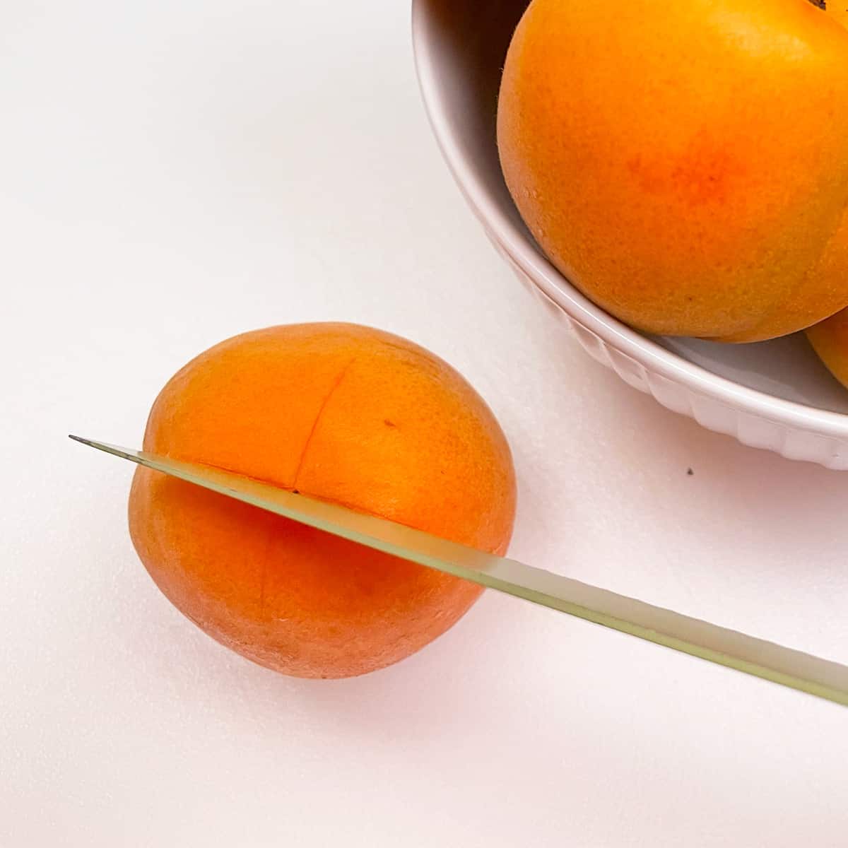 Scoring the top of an apricot before blanching and ice bath.