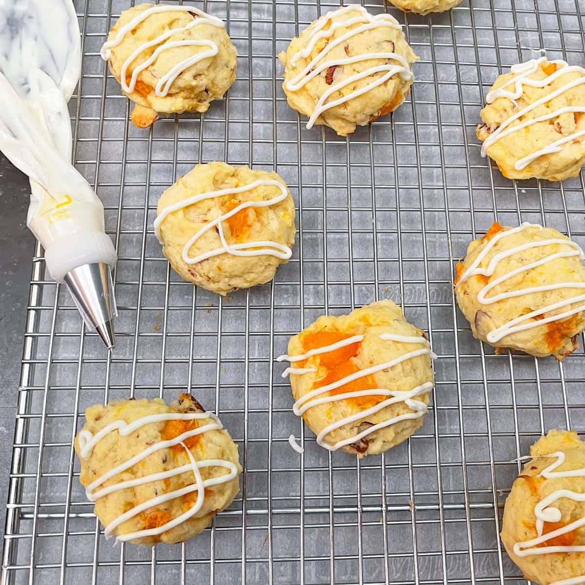 Apricot cookies on cooling rack that have white chocolate drizzled on the tops.