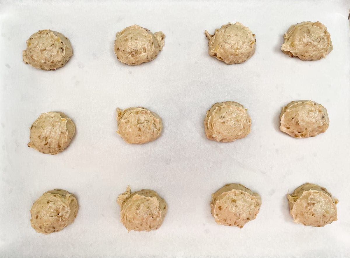 Soft banana cookie dough scooped onto a parchment lined cookie sheet pan.