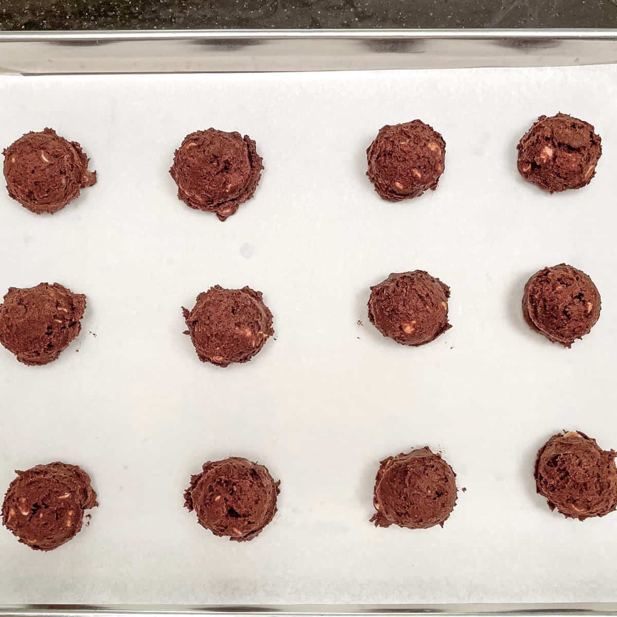 Scooped chocolate cookies on a parchment paper lined sheet pan.