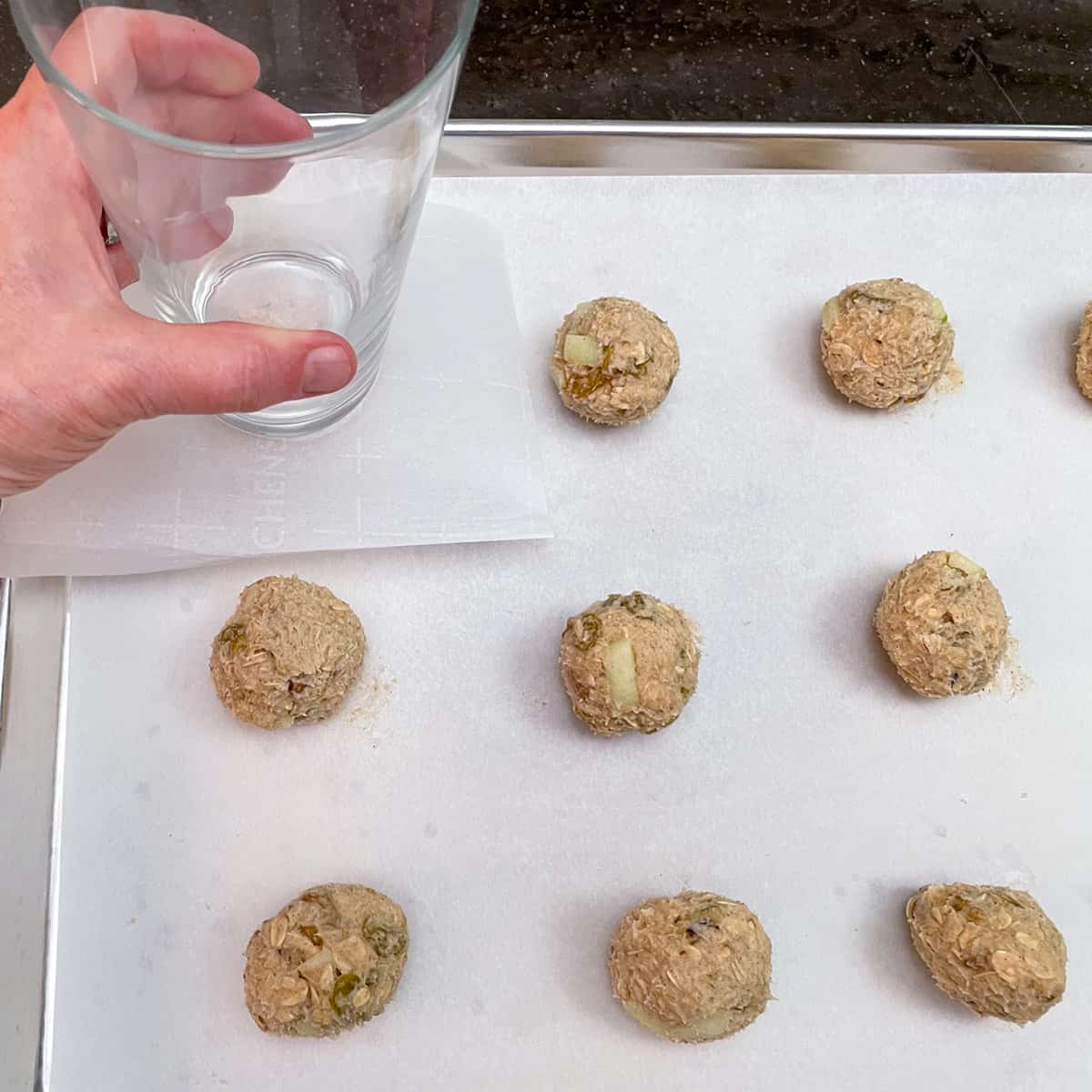 Cookie balls and showing how to flatten the ball using a piece of parchment paper and the bottom of a glass.