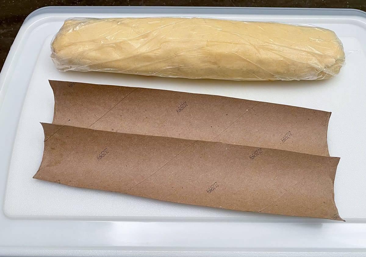 Rolled cookie log wrapped in plastic wrap with the paper towel holder cut lengthwise in half to cradle the log.