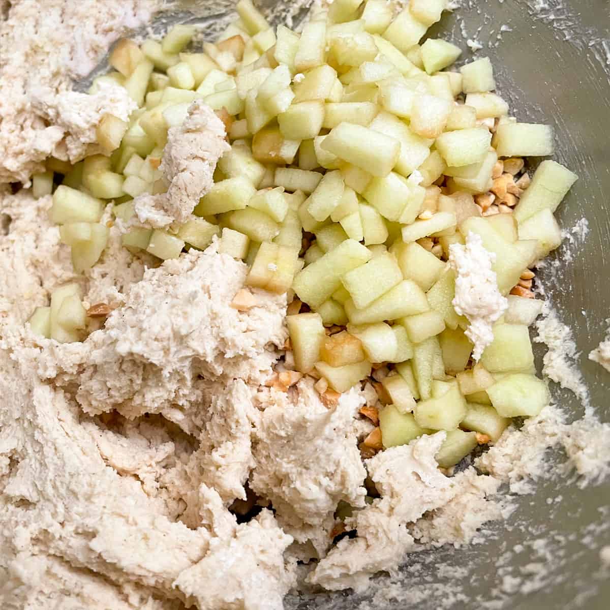 Adding diced apples and chopped peanuts to cookie dough in a mixer bowl.