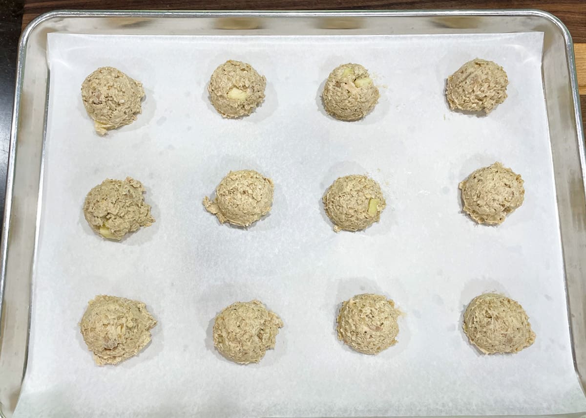 Twelve oatmeal cookie dough on parchment paper ready for the oven.