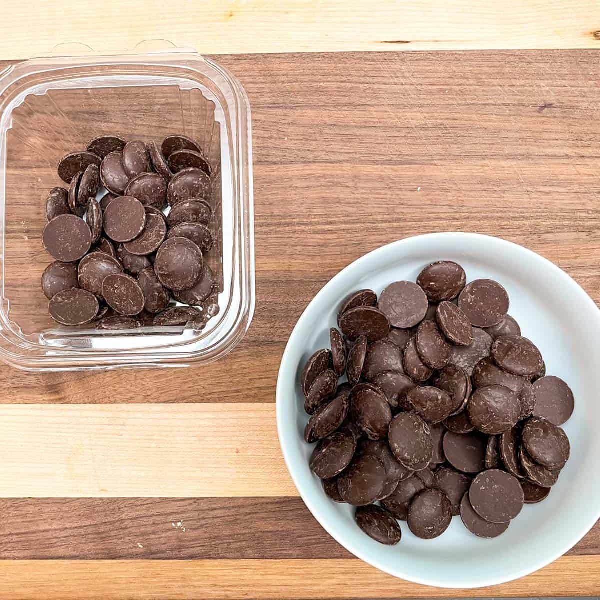 Dark chocolate wafers before they are melted sitting in a white bowl.