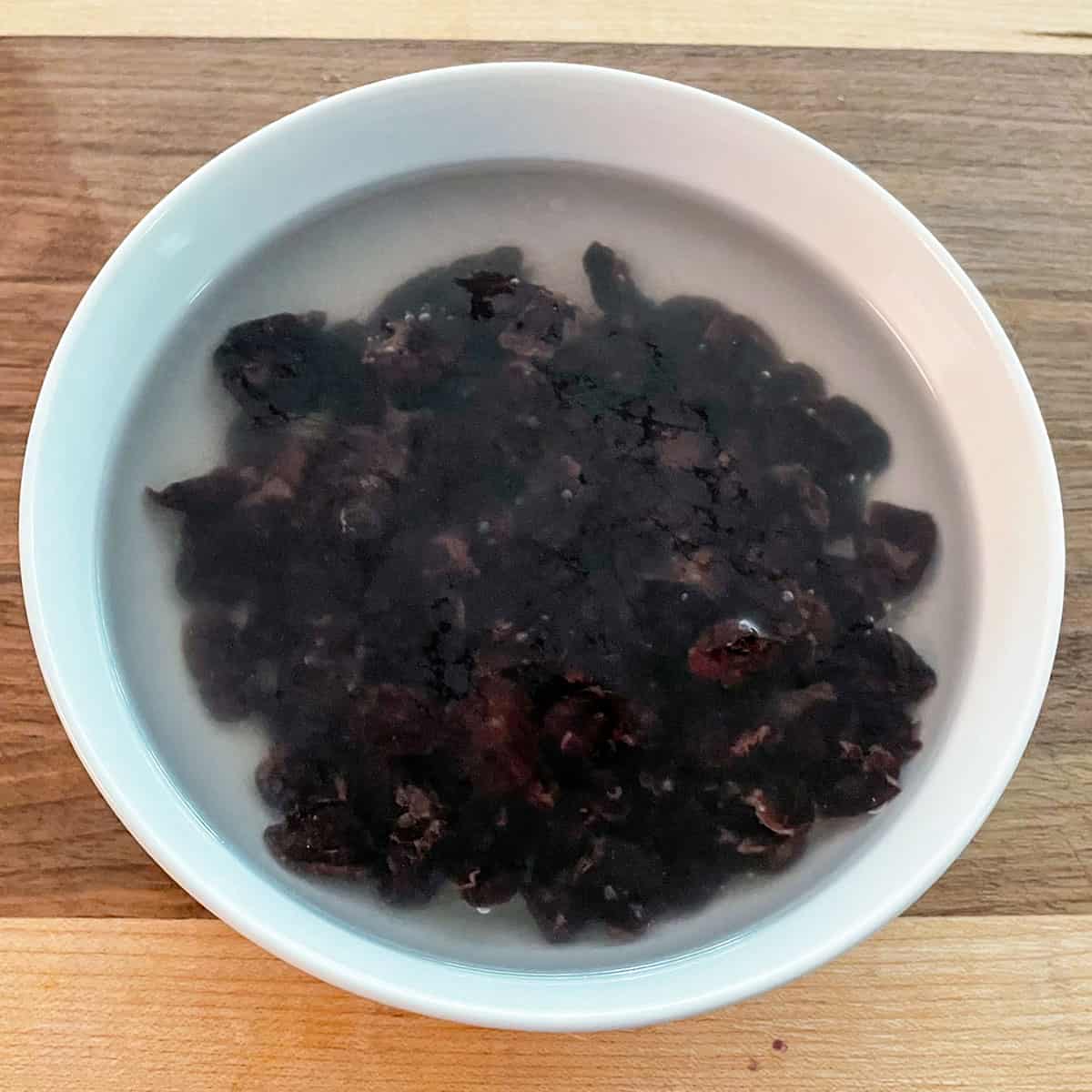 Dried cherries soaking in a white bowl of water and Amoretti.