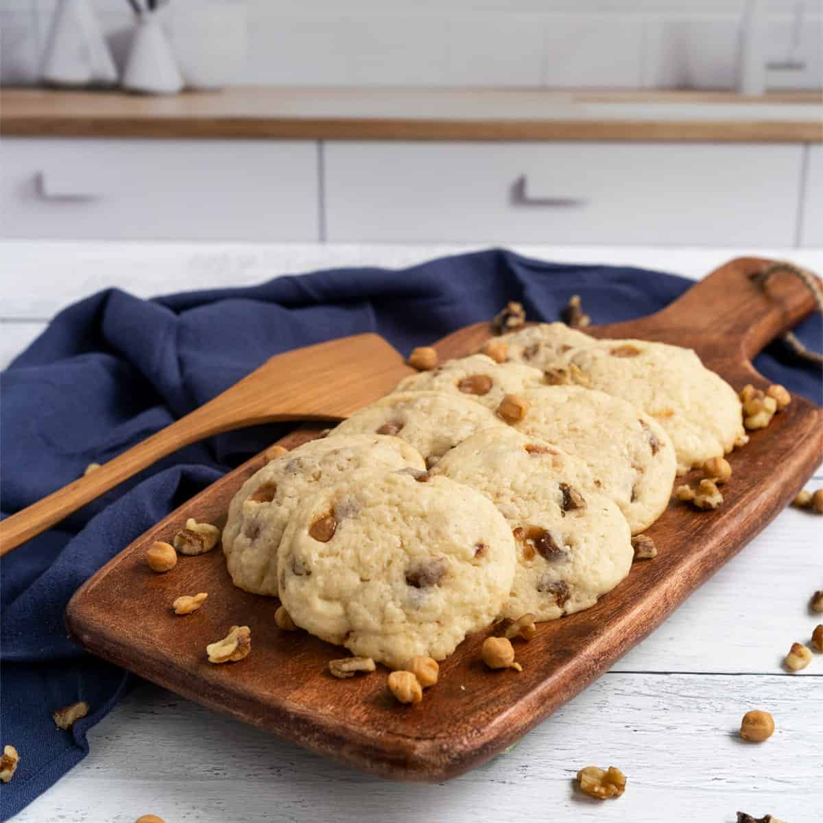 Caramel bits with dates and walnut cookies displayed on a wooden board with a blue towel on the side.