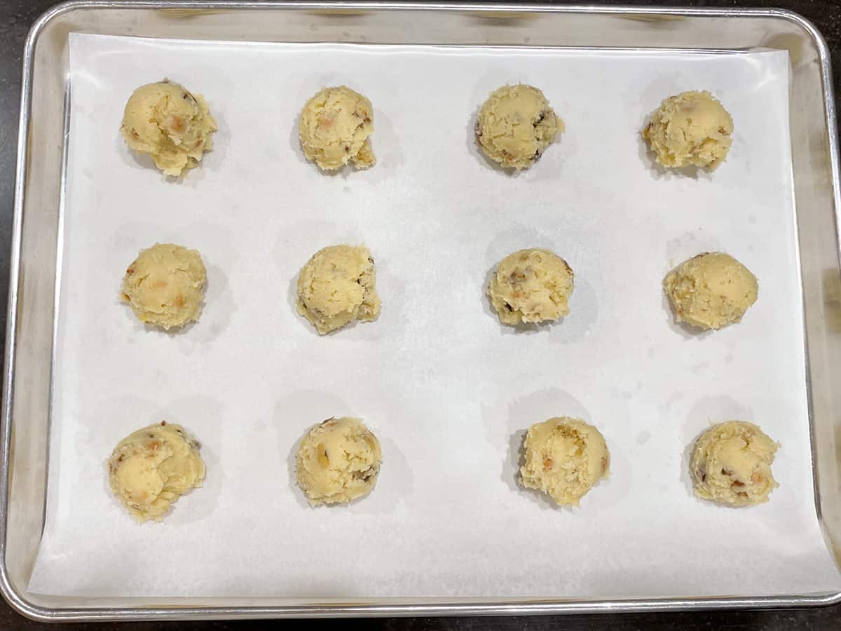 twelve mounds of cookie dough on parchment paper ready for the oven.