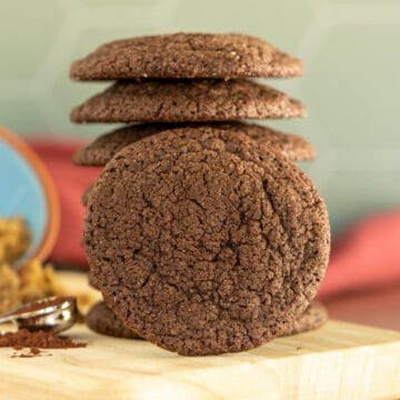 A stack of chocolate sugar cookies on a light-colored board with a raspberry cloth behind the stack.