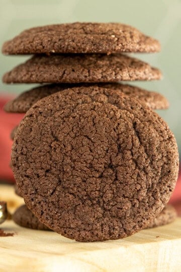 A stack of chocolate sugar cookies on a light-colored board with a raspberry cloth behind the stack.