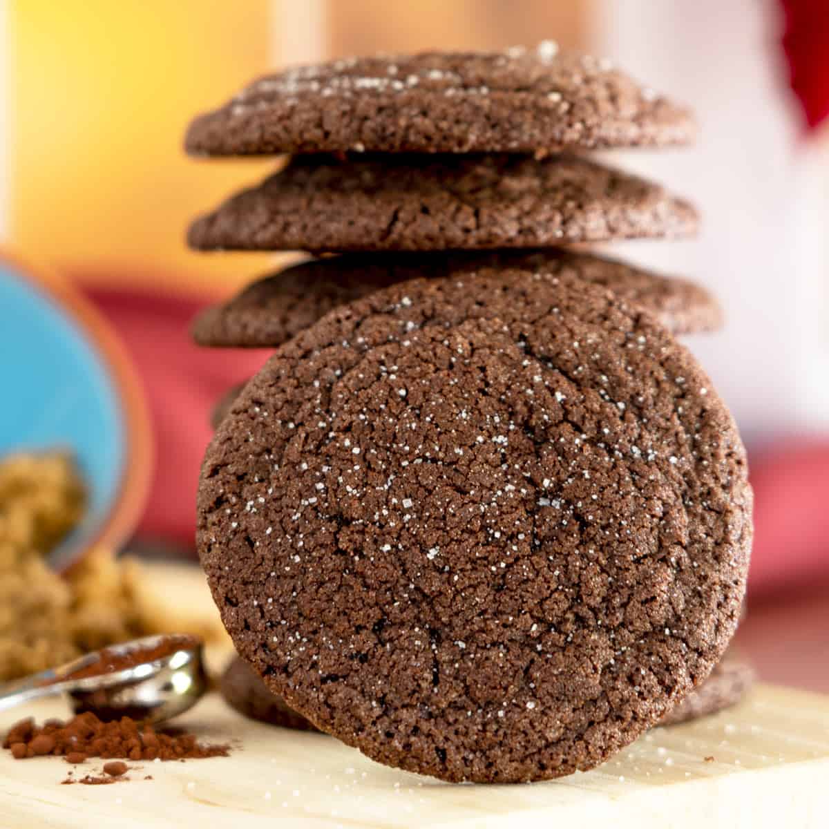Chocolate sugar cookies stacked with a single cookie facing you that has some white sugar springled on it.