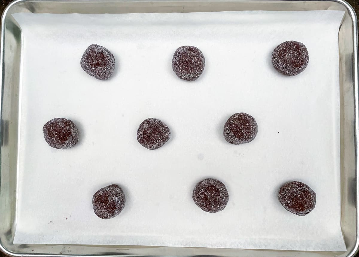 Nine cookie balls rolled in sugar and place on a parchment lined cookie sheet pan.
