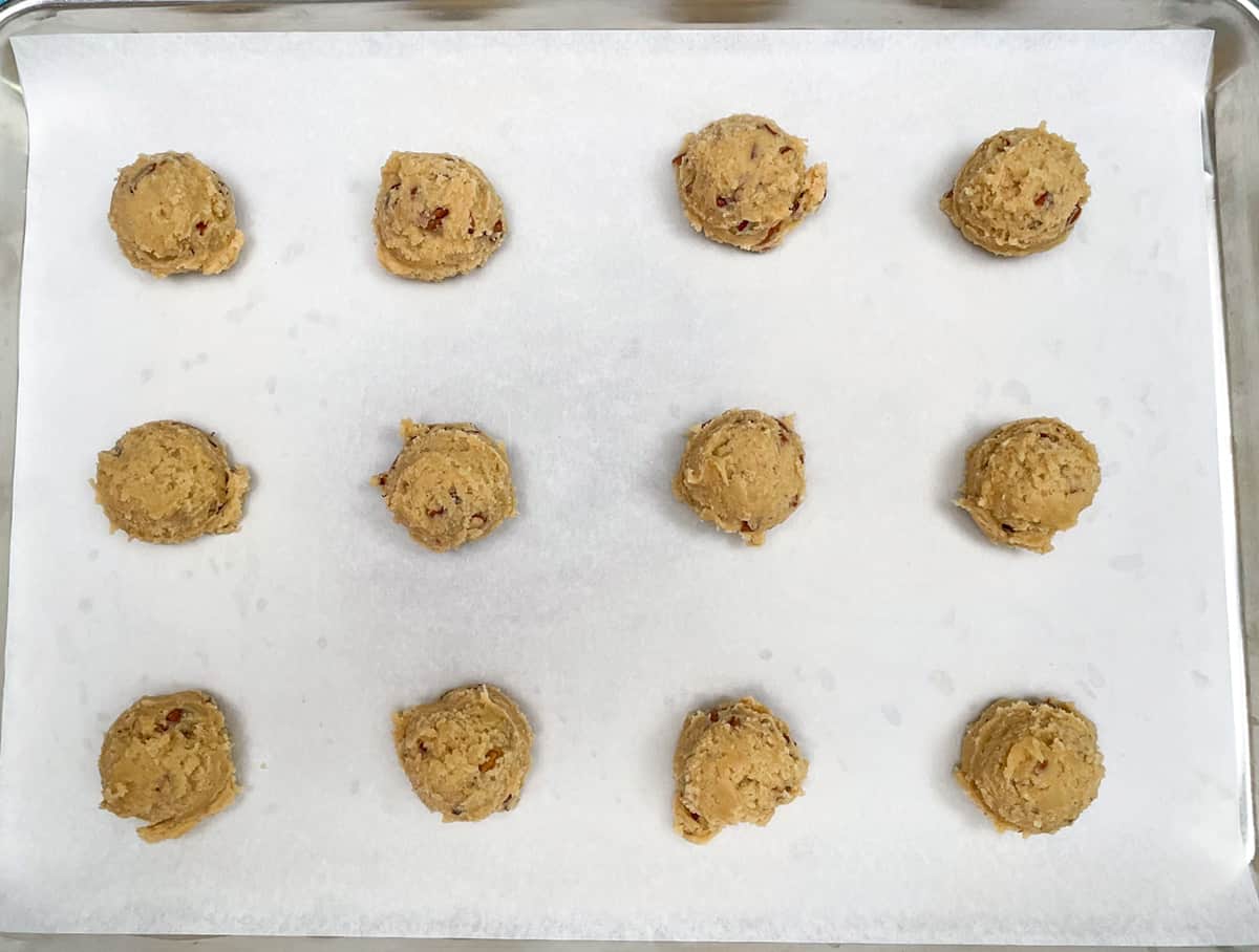 Twelve maple cookies scooped and sitting on a parchment-lined cookie sheet pan.