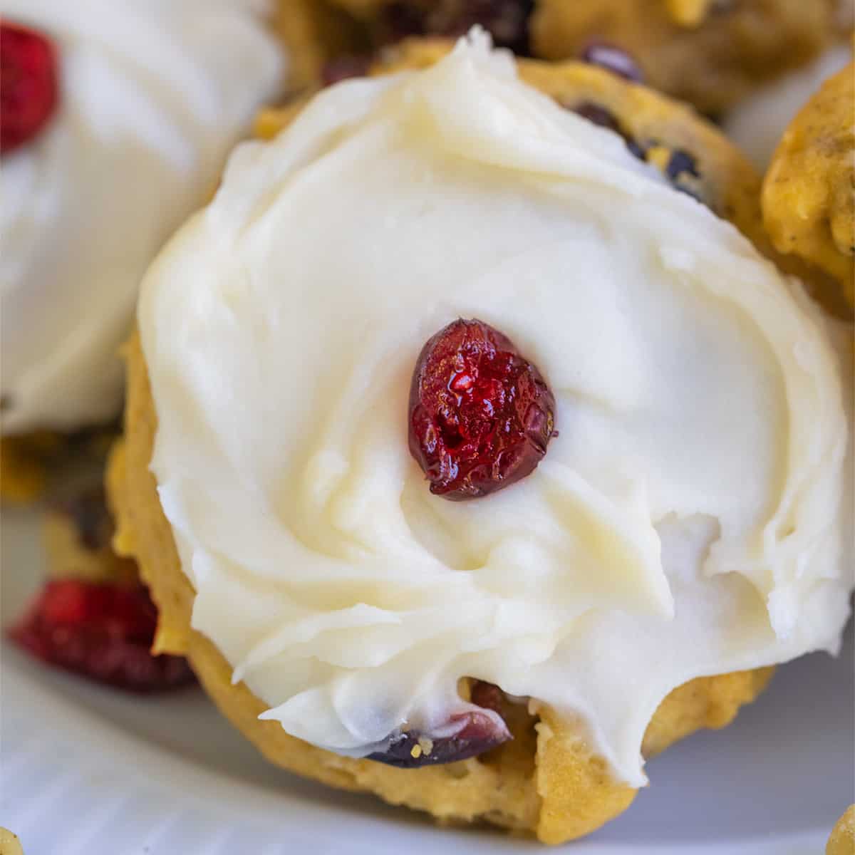Pumpkin cranberry cookies and cream cheese icing with a single cranberry in the middle.
