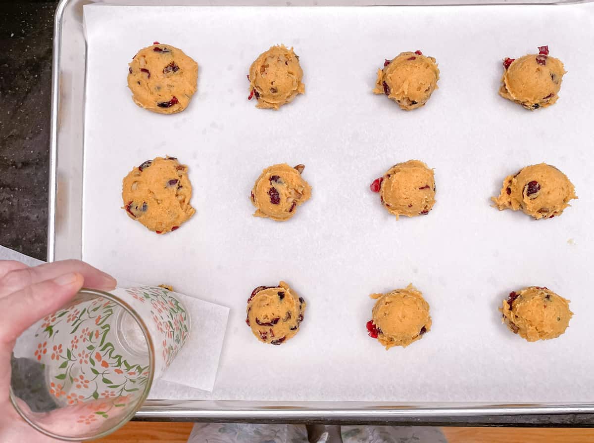 How to flatten a cookie mound with a piece of parchment paper and the bottom of a water glass