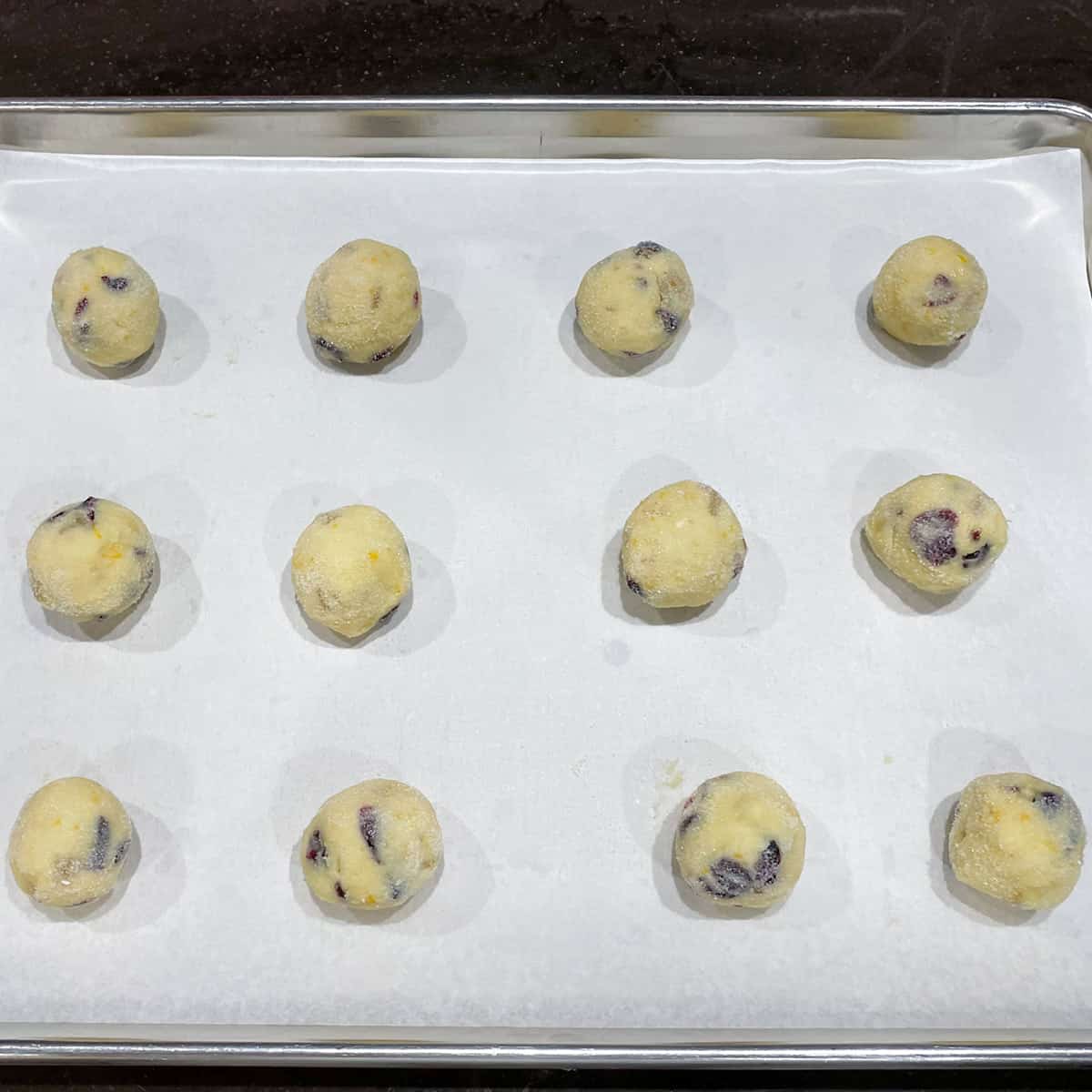 Twelve rolled cookies dough balls in super fine sugar on a parchment lined cookie sheet pan.