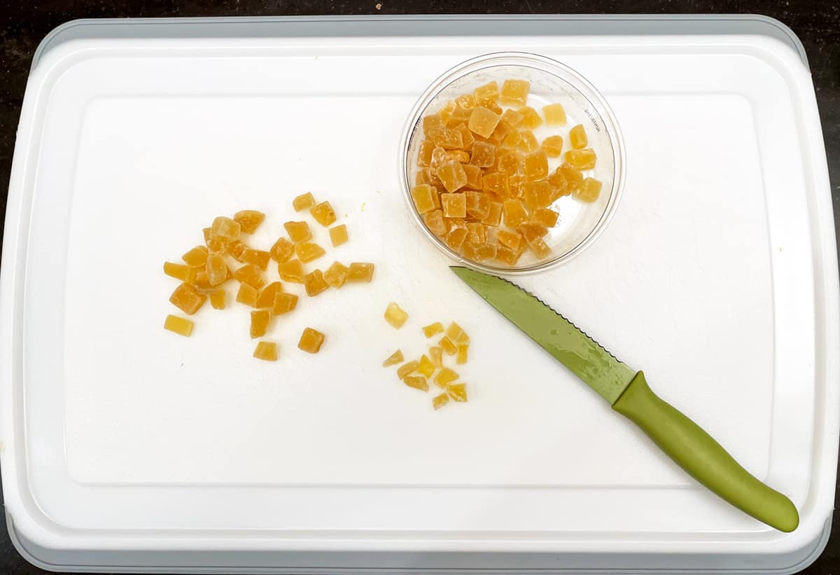 Dicing crystallized ginger into small pieces on a white cutting board.
