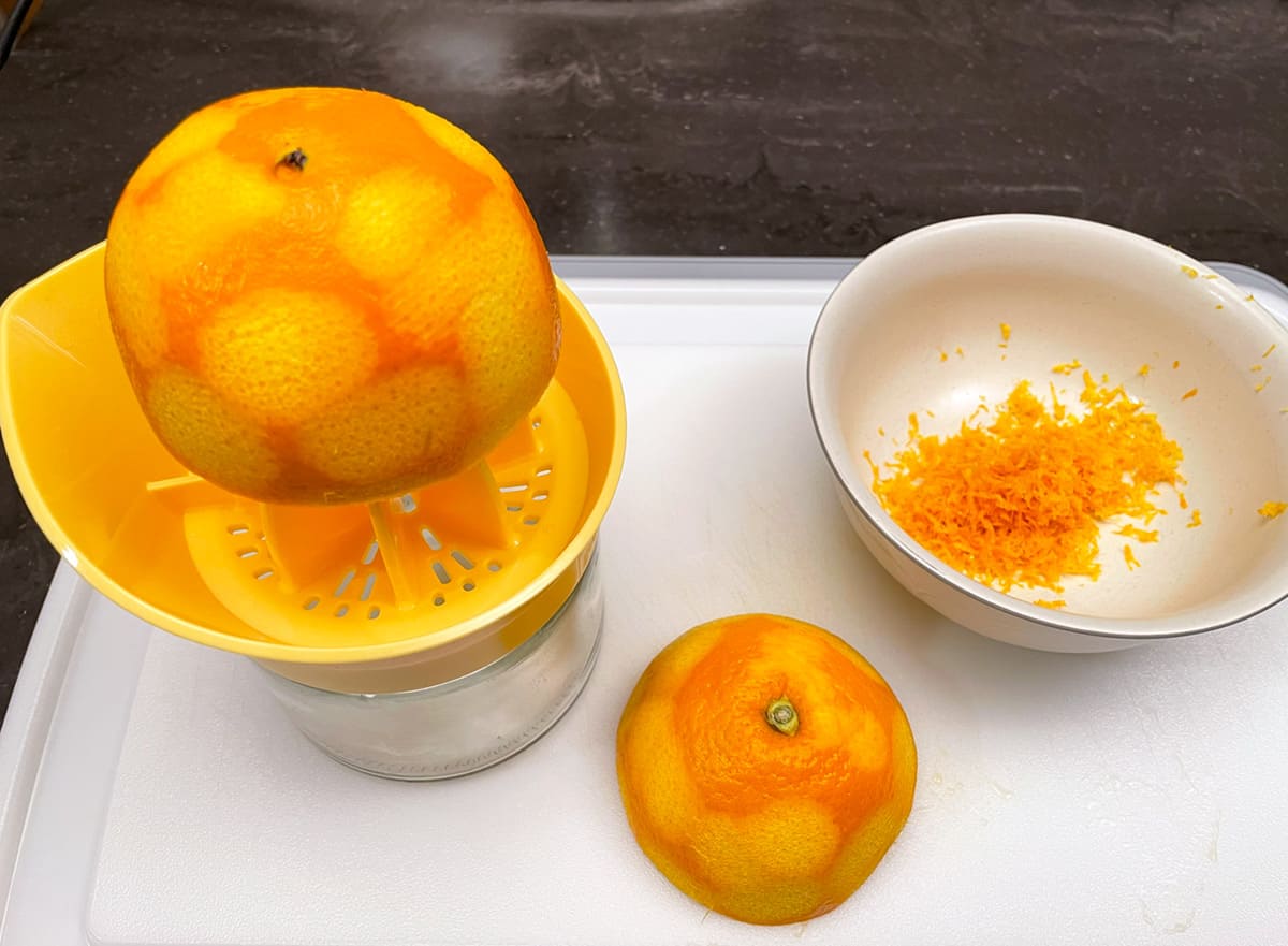 Zest in a bowl and half orange on a juicer ready to be turned to get juice.