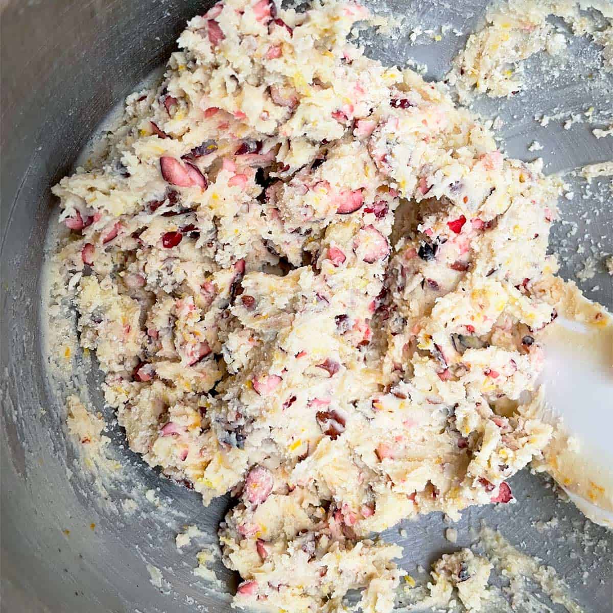 Sortbread dough with cranberry and orange with pecan pieces in a mixer bowl.