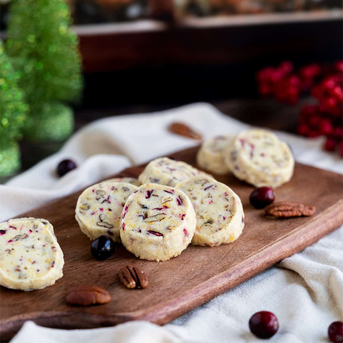Fresh cranberr orange pecan shortbread cookies on a wooden board with whole cranberries and pecans.