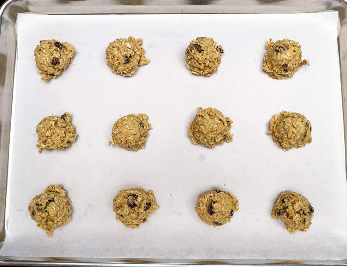 Parchment lined cookie sheet pan with twelve cookie mounds ready for the oven.