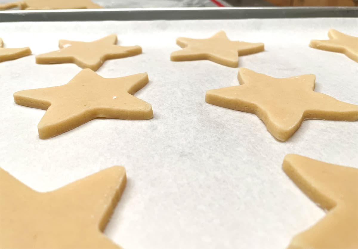 Sugar cookies that are cut out into stars on a parchment lined sheet pan.