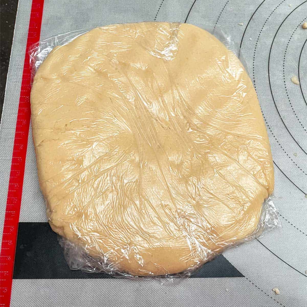 Half the cookie dough flattened to a disk and wrapped in plastic wrap.