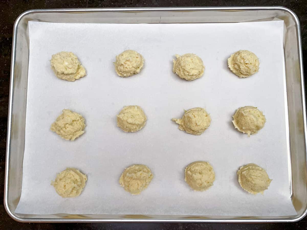 Twelve scoops of key lime cookie dough on a parchment lined sheet pan.