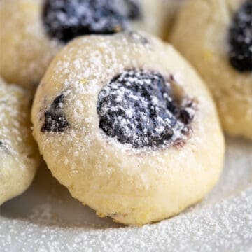 Single blueberry with blueberry jam cookie with powdered sugar sprinkled on top.