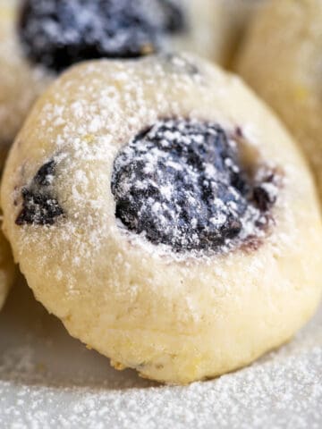 Single blueberry with blueberry jam cookie with powdered sugar sprinkled on top.
