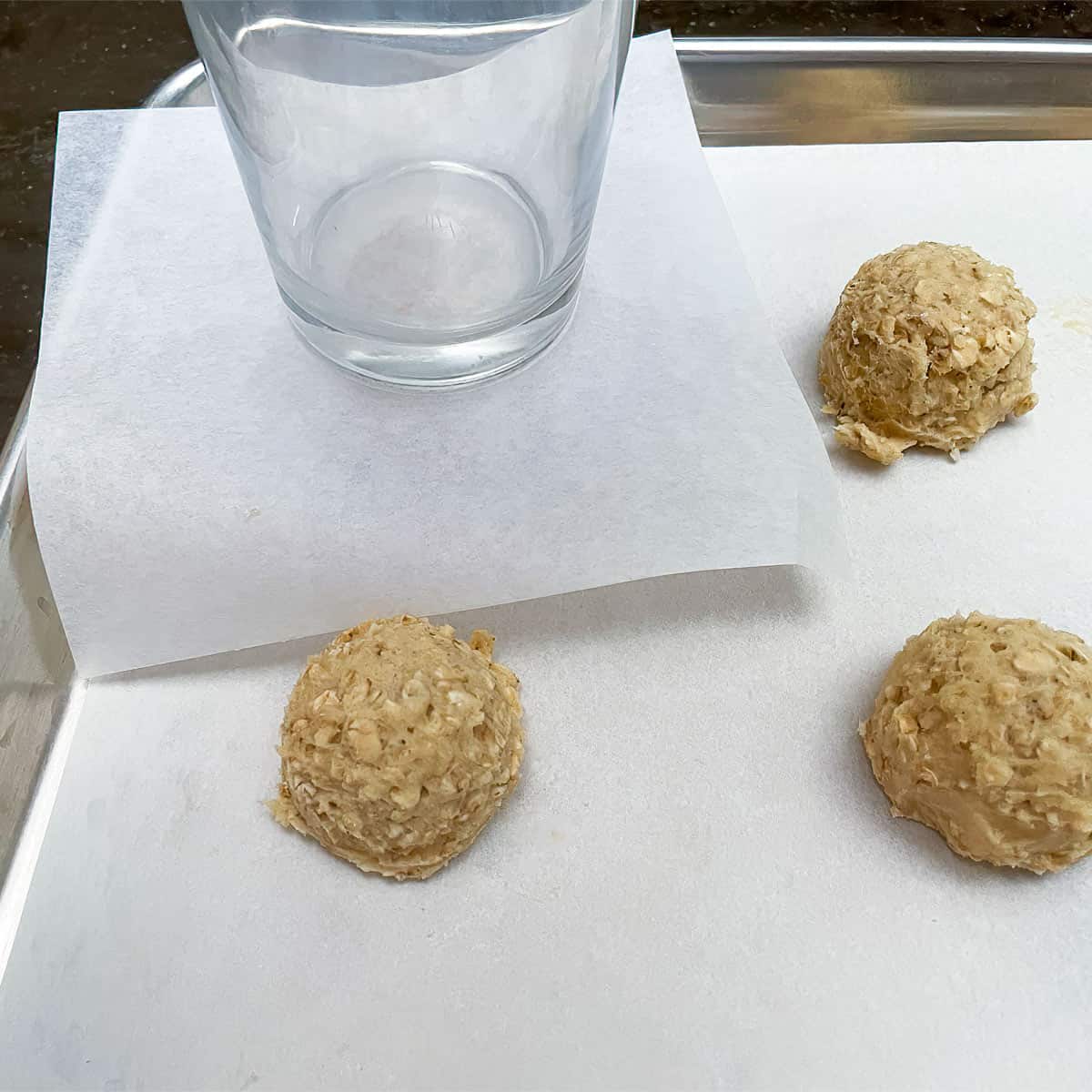 Using a square piece of parchment paper between cookie mound and the bottom of the glass to flatten mounds.