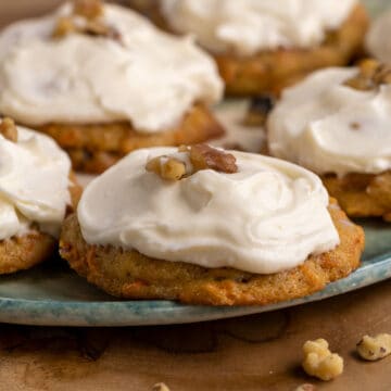 Close up of the cookie that shows small pieces of carrot and is topped with a creamy cream cheese icing and walnut bits.