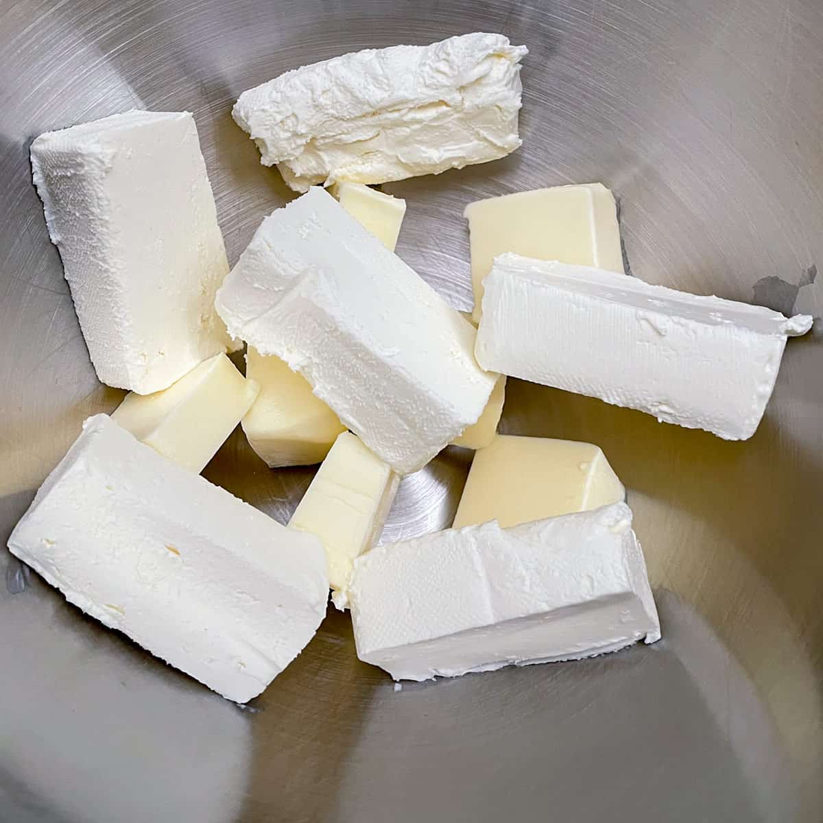 Cutting up butter and cream cheese into a mixer bowl.