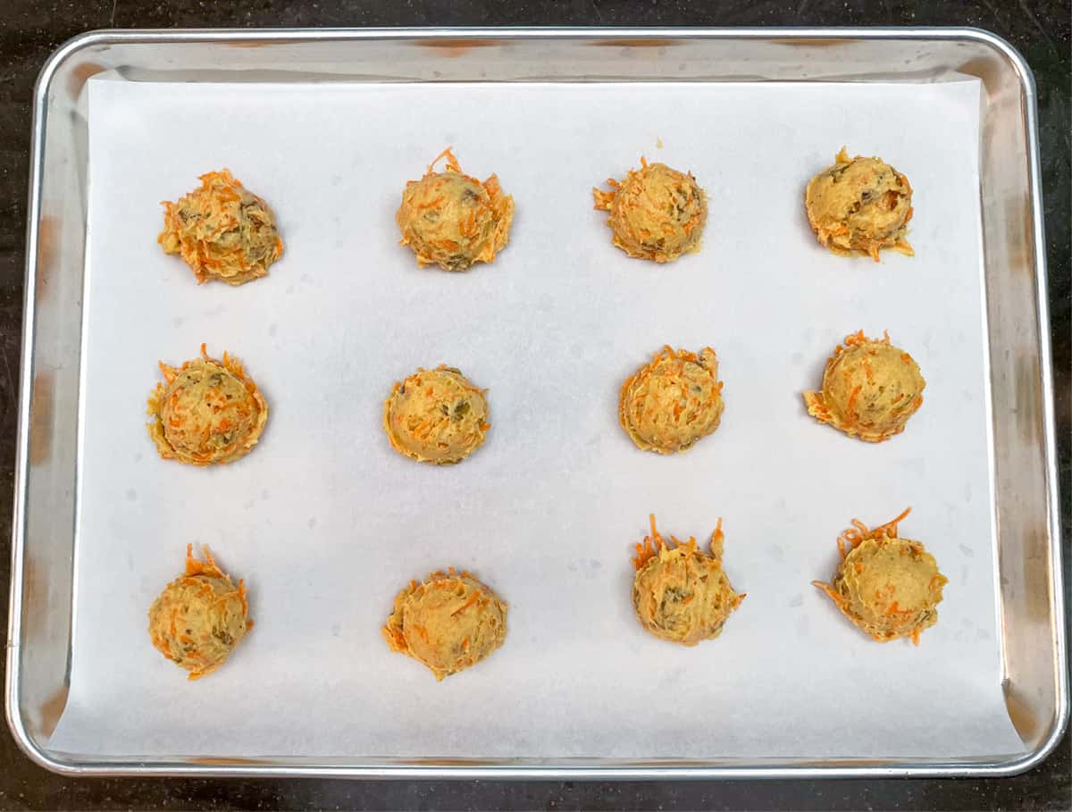 Carrot cake cookie dough scooped onto parchment paper on a sheet pan.