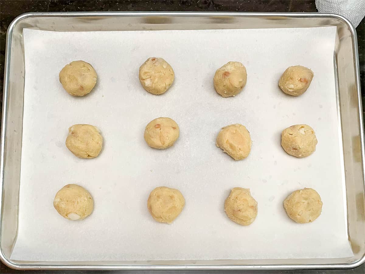 Twelve rolled cookie balls on a parchment lined sheet pan.