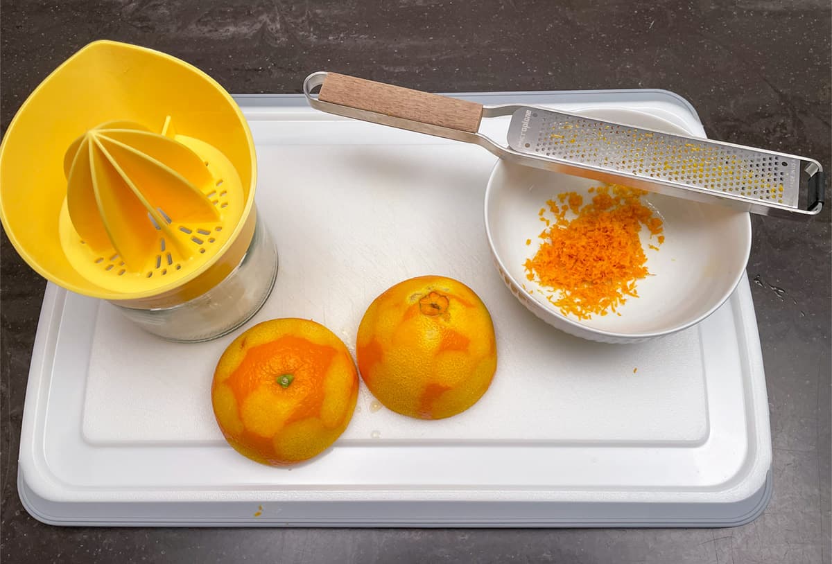 Zesting and juicing an orange on a cutting board.