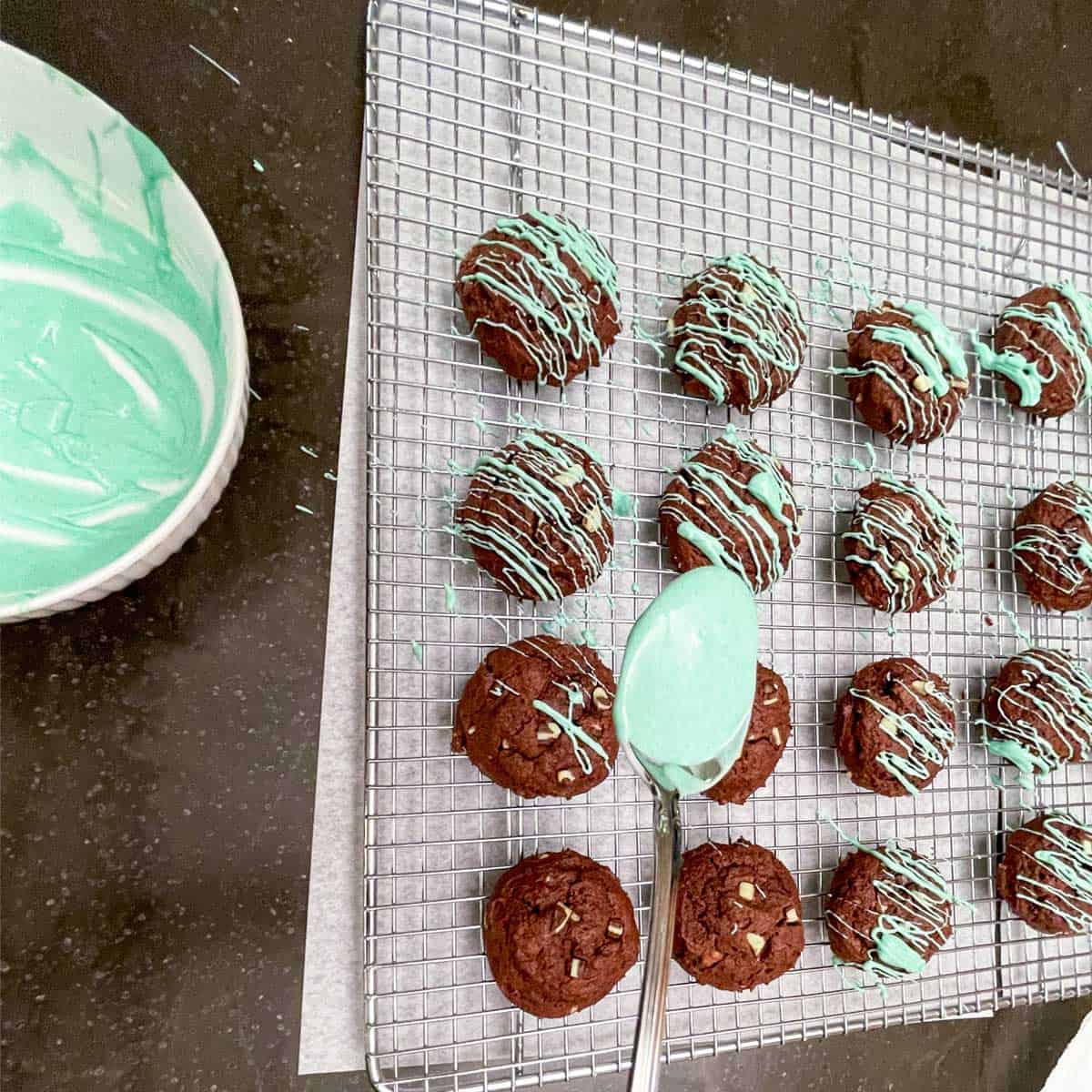 Green colored white chocolate in a spoon going back and forth to drizzle over the tops of the baked cookies.
