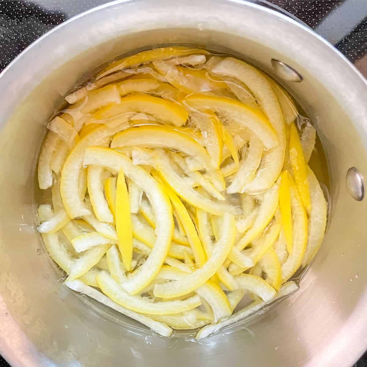 Covering blanched lemon peel with simple syrup in a saucepan.
