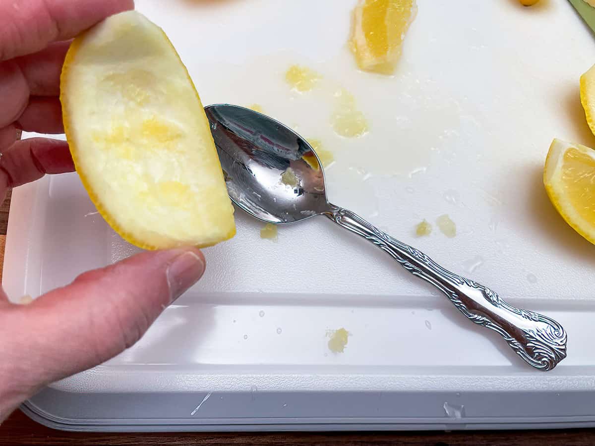 Scraping the inside of the lemon with a spoon.