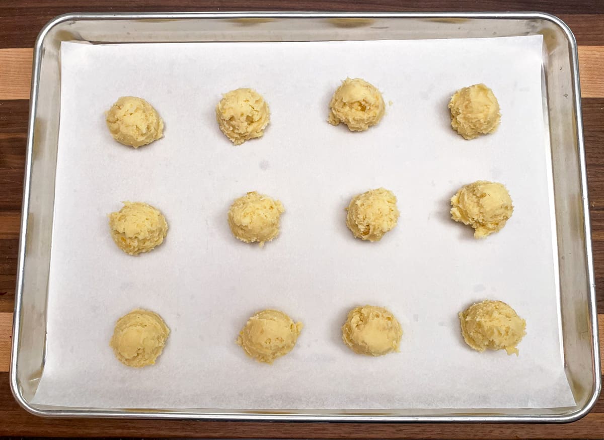 Twelve cookie mounds scooped onto a parchment-lined cookie sheet pan.