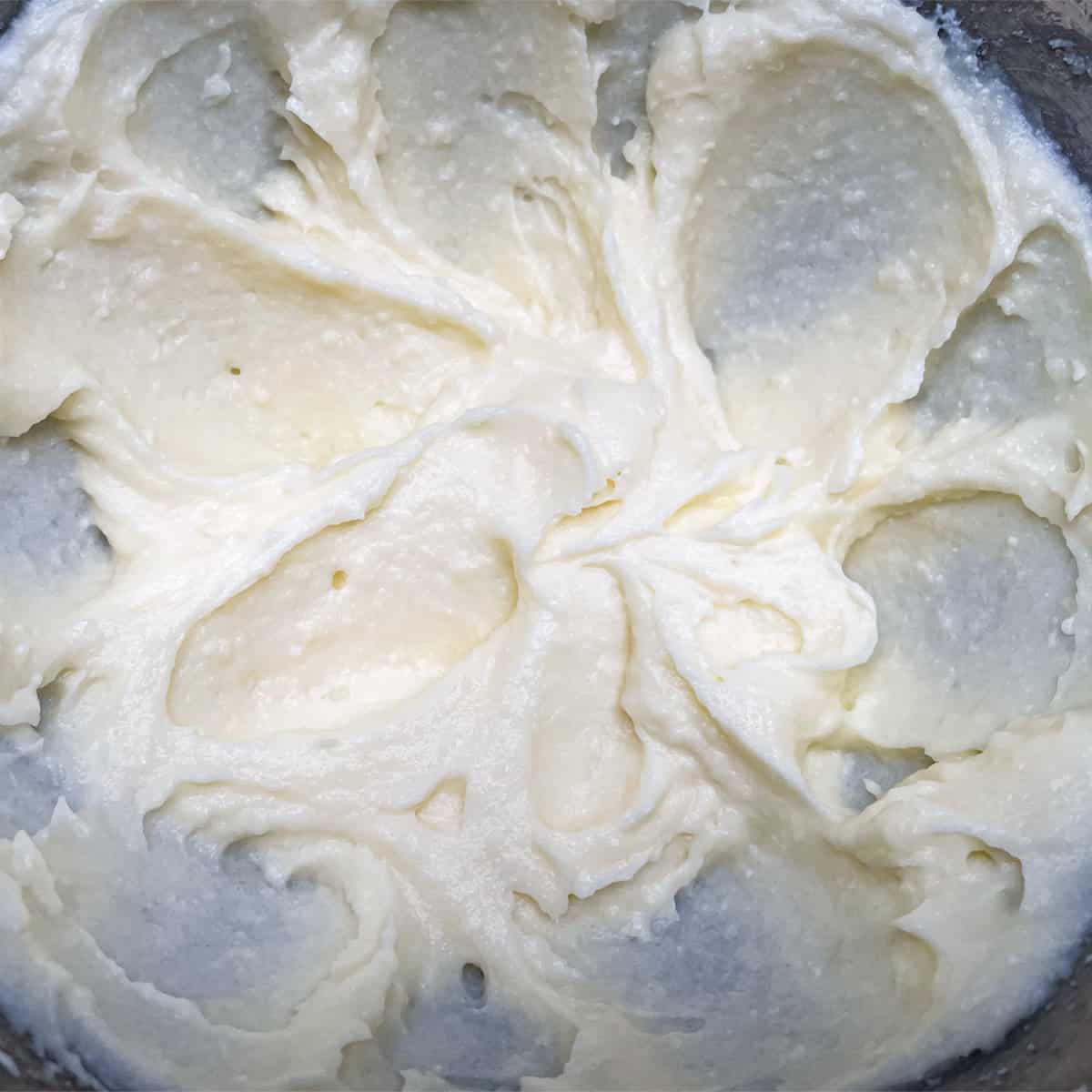 The creamy looking mixture of butter, sugar, and ricotta together in a mixer bowl.