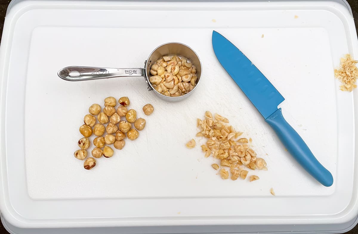 Chopping whole hazelnuts into smaller pieces on a cutting board.