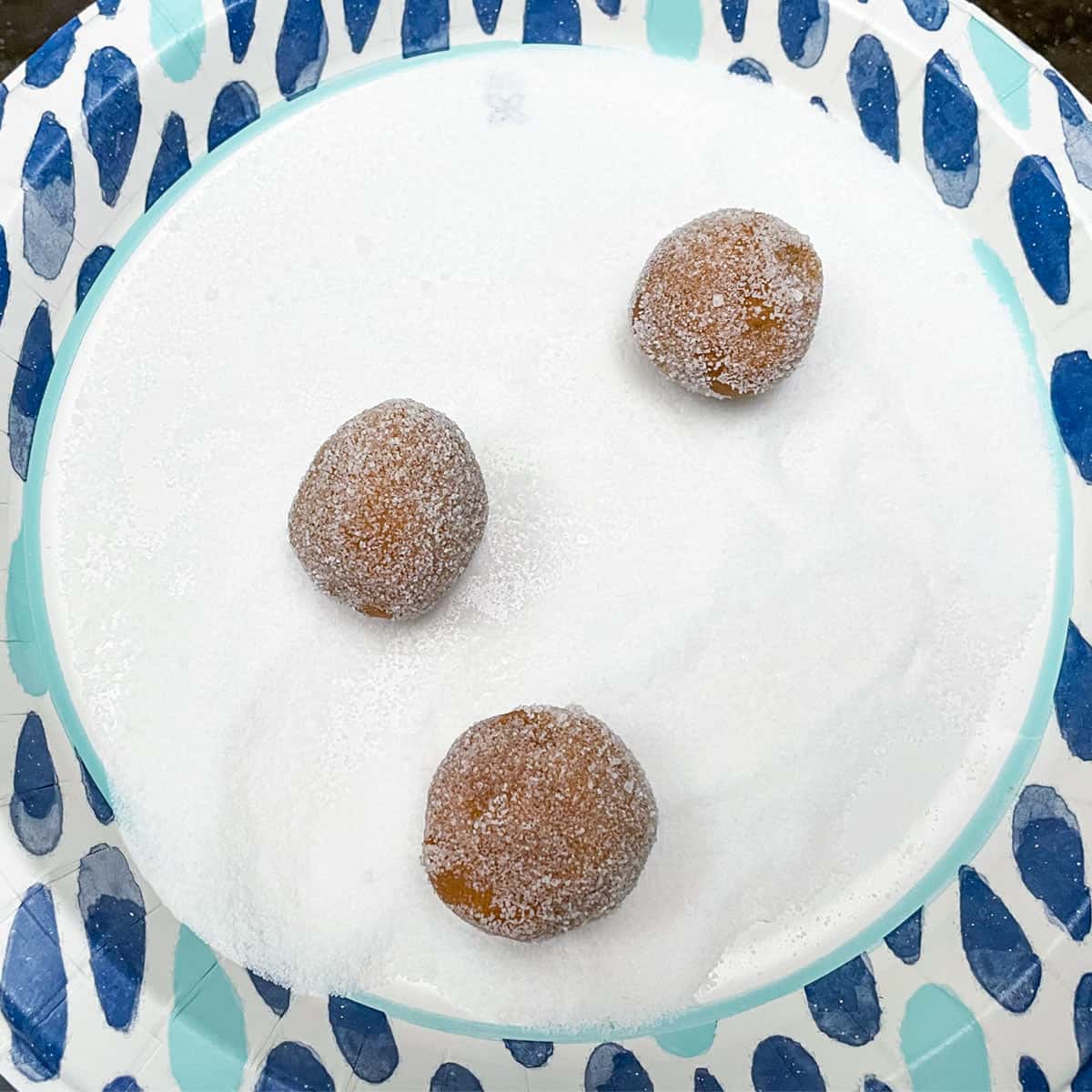 Rolling cookie balls on a plate with sugar.