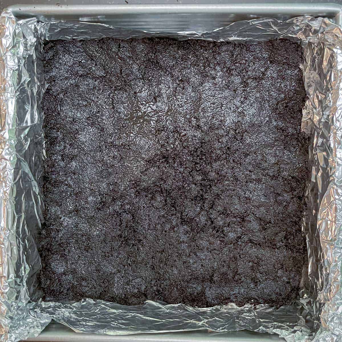 Oreo crust pressed down to cover the bottom of the tinfoil-lined pan.